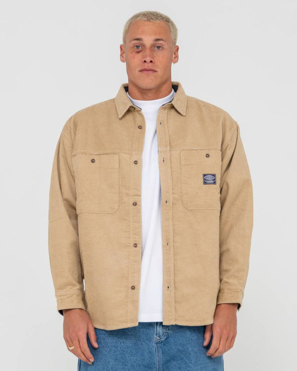 Men's beige corduroy button-up jacket with two chest pockets, worn over a white t-shirt and blue jeans for a casual look.