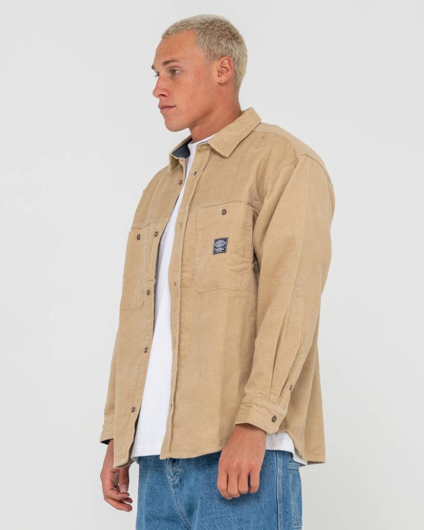 Side view of a men's beige corduroy button-up jacket with front pockets, worn over a white t-shirt and blue jeans.