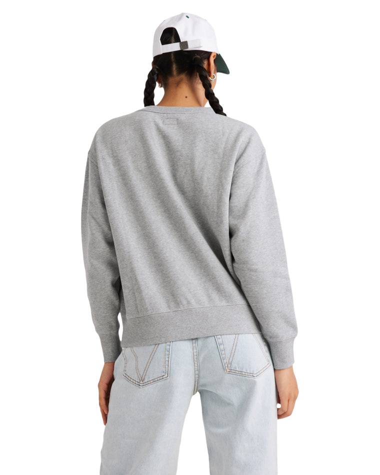 Back view of a woman wearing a grey RVCA fleece crew with ribbed hem and cuffs, paired with light-wash jeans and a white cap.