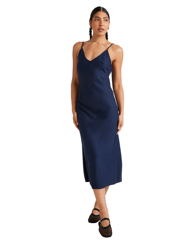 Navy blue slip dress with a sleek silhouette, delicate spaghetti straps, and a midi length, styled with black strappy flats.