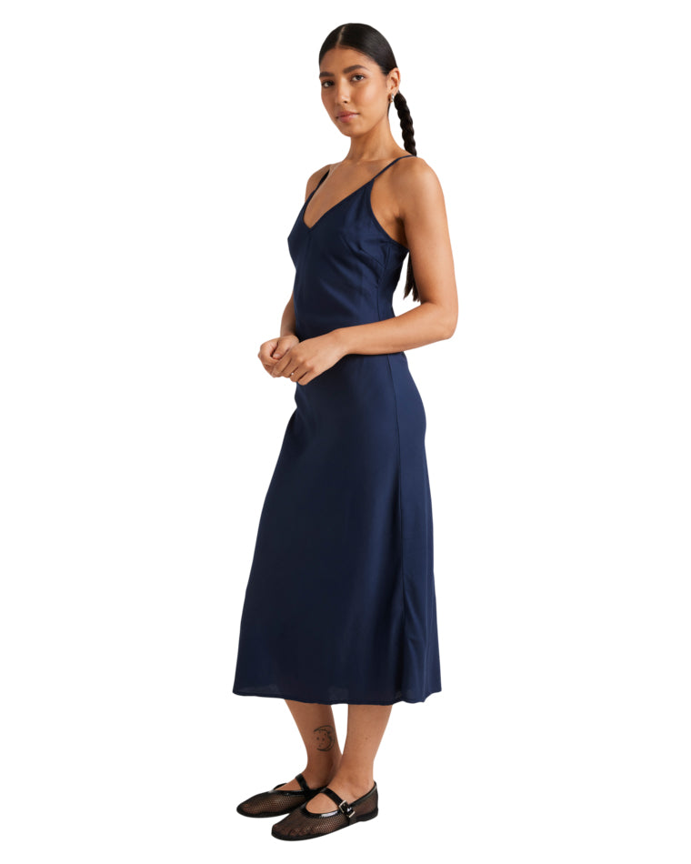 Side view of a navy blue slip dress with a V-neckline and midi-length silhouette, styled with black Mary Jane flats.