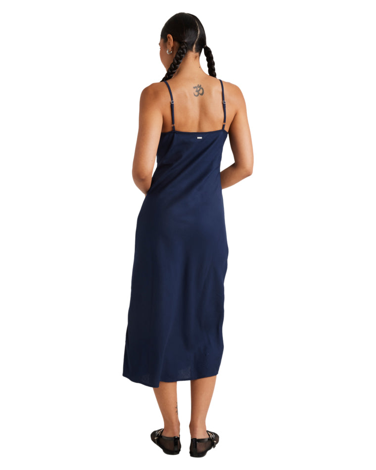 Back view of a navy blue slip dress featuring adjustable spaghetti straps and a midi-length design, styled with black flats.