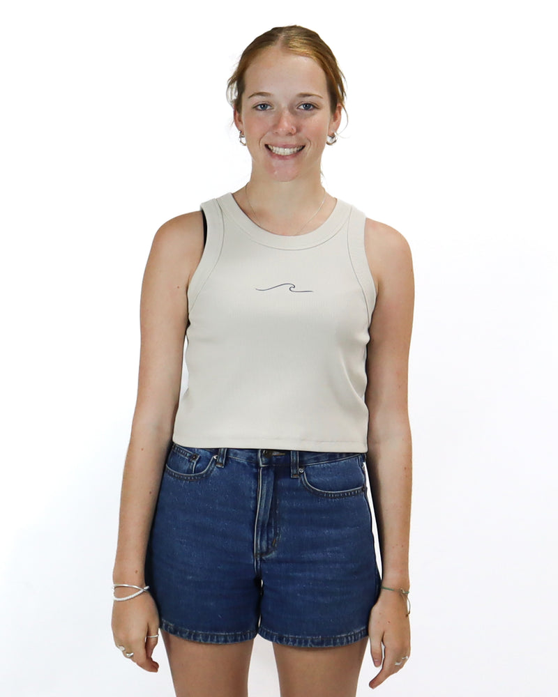 Beige cropped tank top with a small wave design on the chest, paired with high-waisted dark denim shorts.