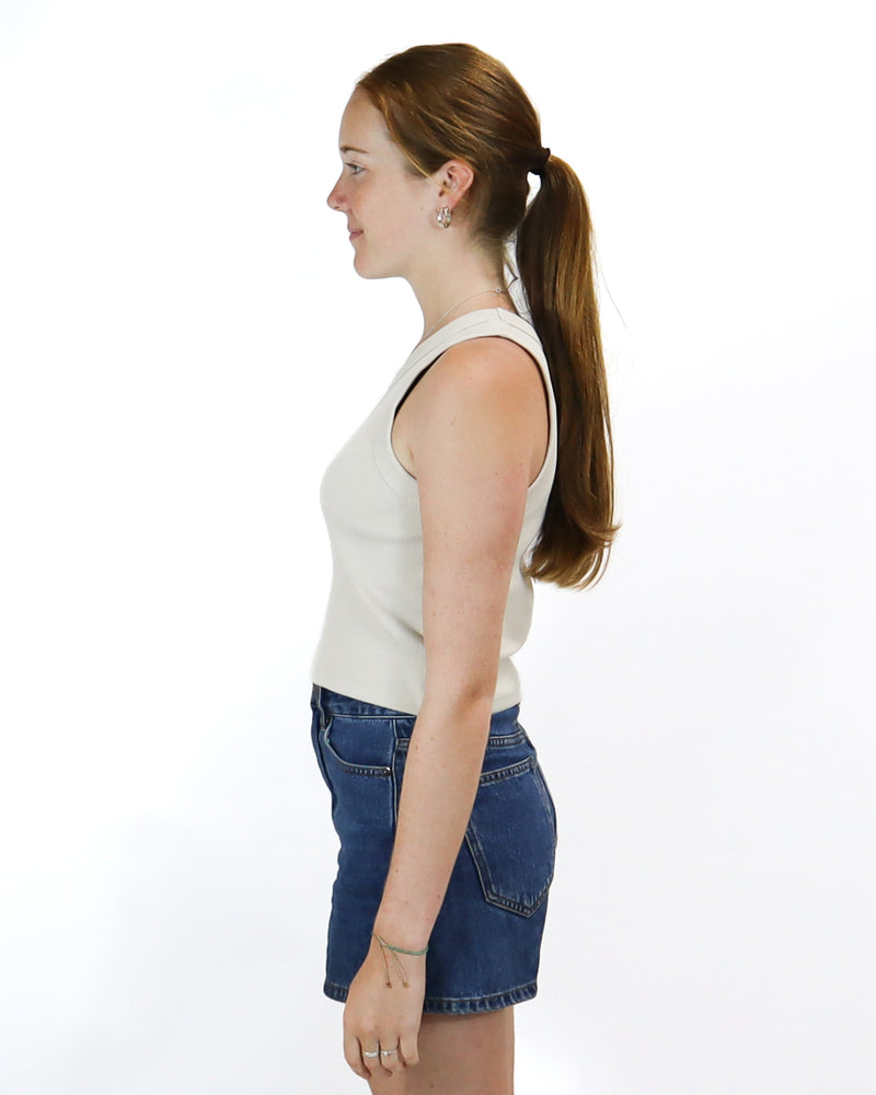 Side view of a beige cropped tank top with a fitted design, paired with high-waisted dark denim shorts.