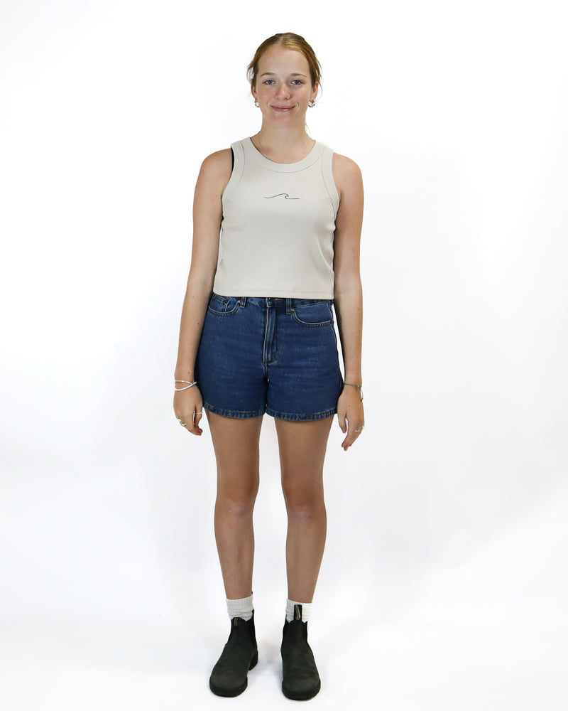 Beige cropped tank top with subtle wave design on the chest, paired with high-waisted denim shorts and black ankle boots.