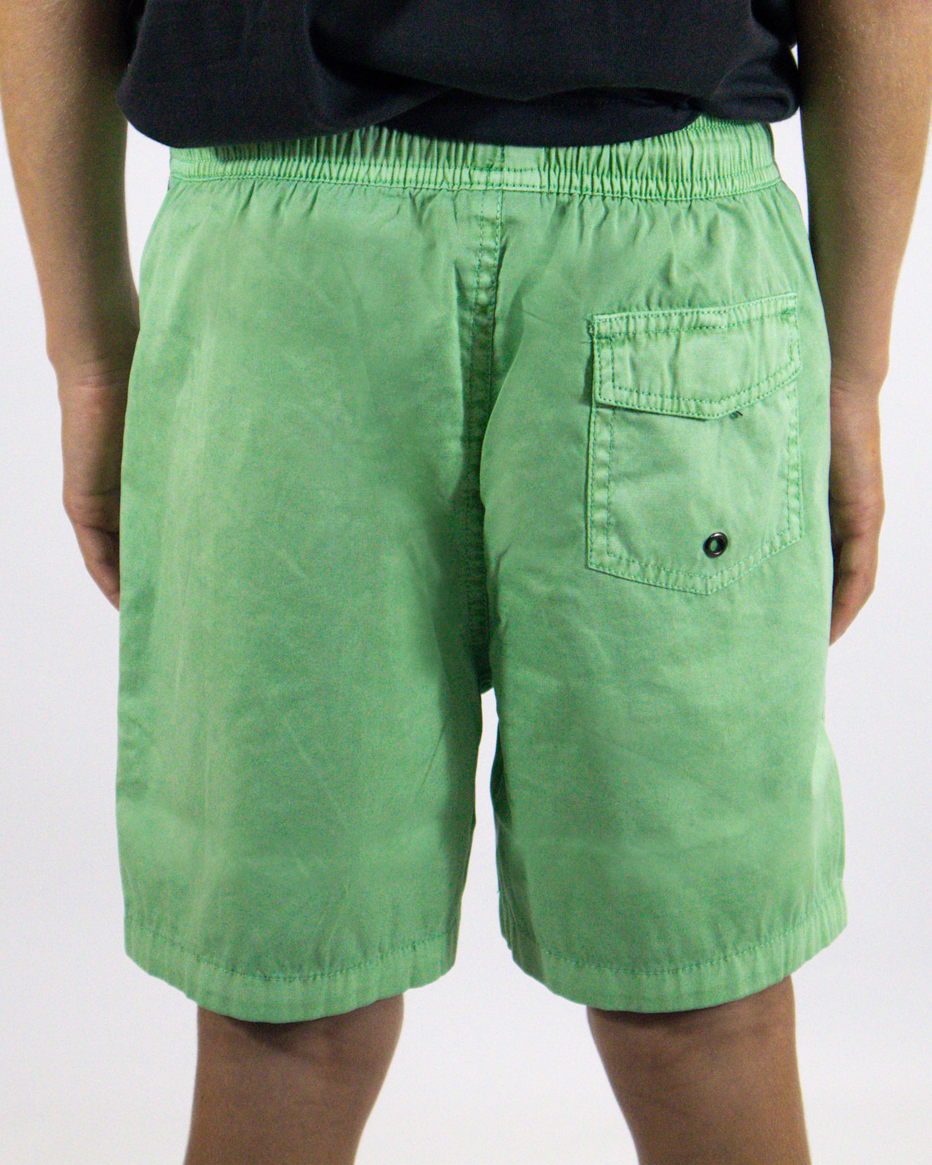 Back view of green shorts featuring flap pocket and elastic waistband.