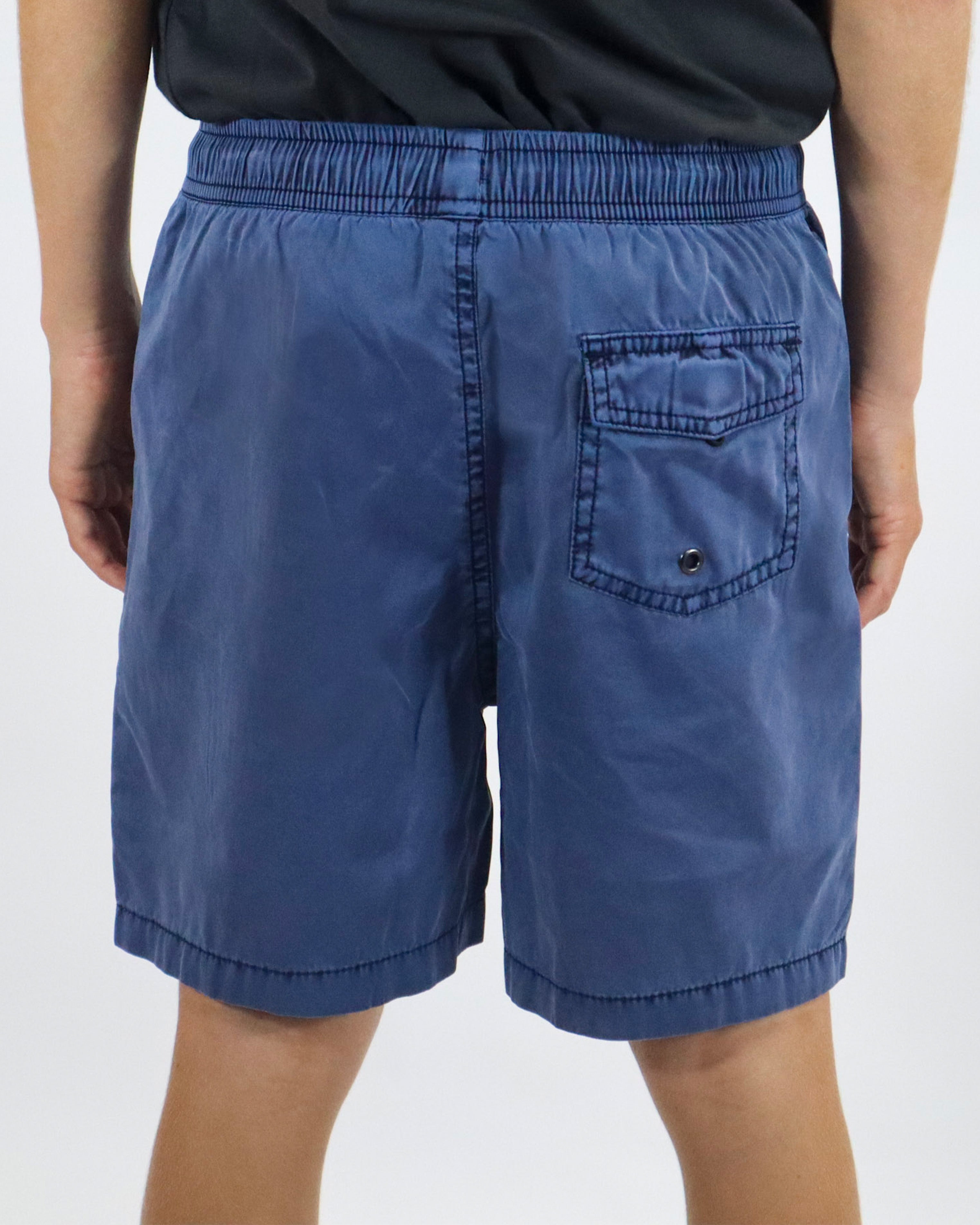 Back view of blue boardshorts featuring a flap pocket with button closure on the right side