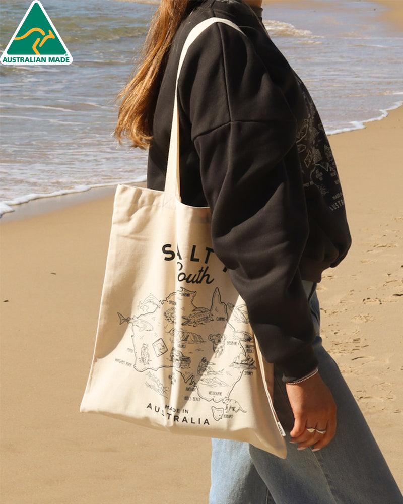 Canvas Salty South tote bag with black illustrated Australia map print, worn over the shoulder at the beach
