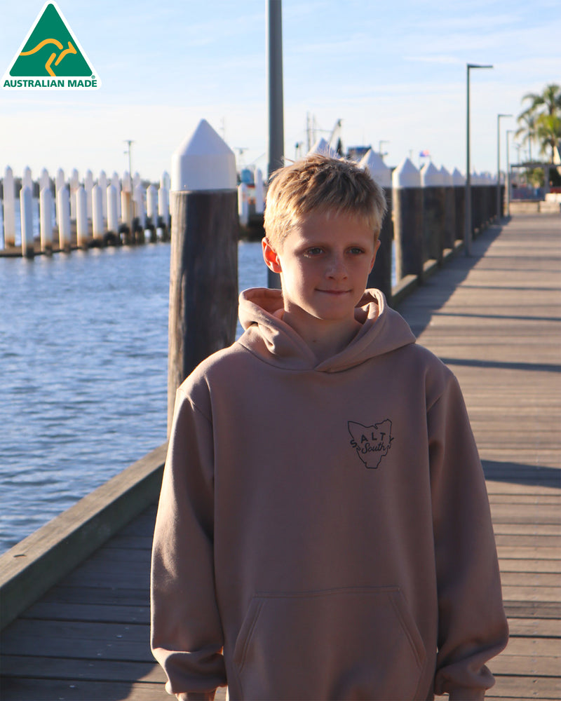 Kids tan Salty South hoodie with Tasmania chest print, photographed on a boardwalk by the water