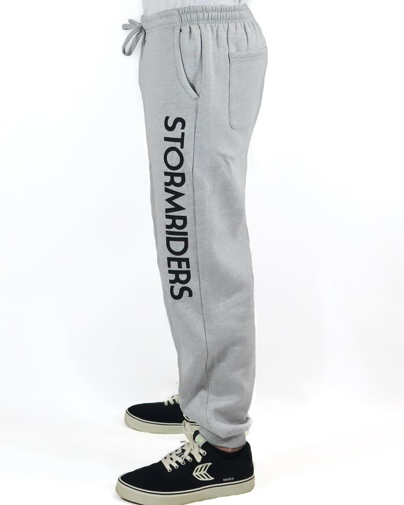 Side view of light grey Stormriders track pants with bold black logo.