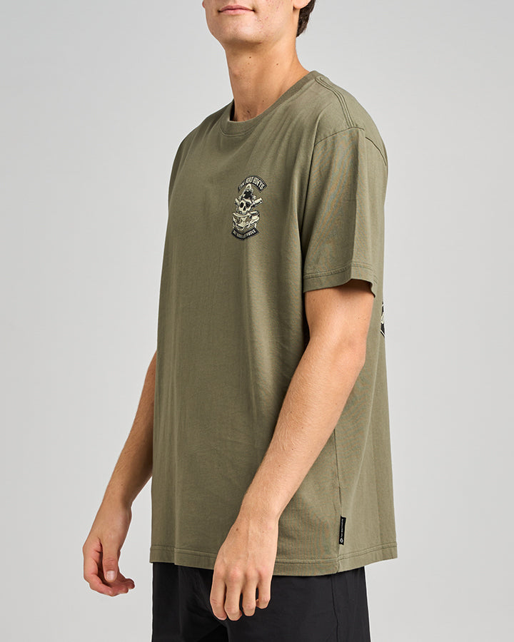 A model wearing an olive green graphic t-shirt with a skull design on the chest, shown from the side.