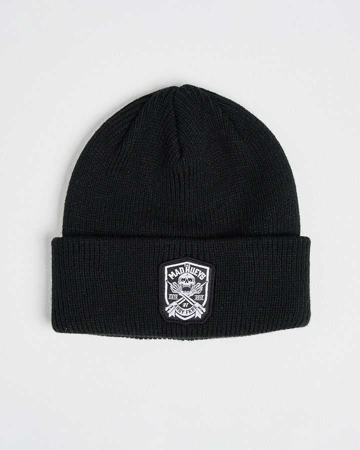 Black ribbed beanie with The Mad Hueys embroidered logo patch on the cuff, laid flat on a white background.