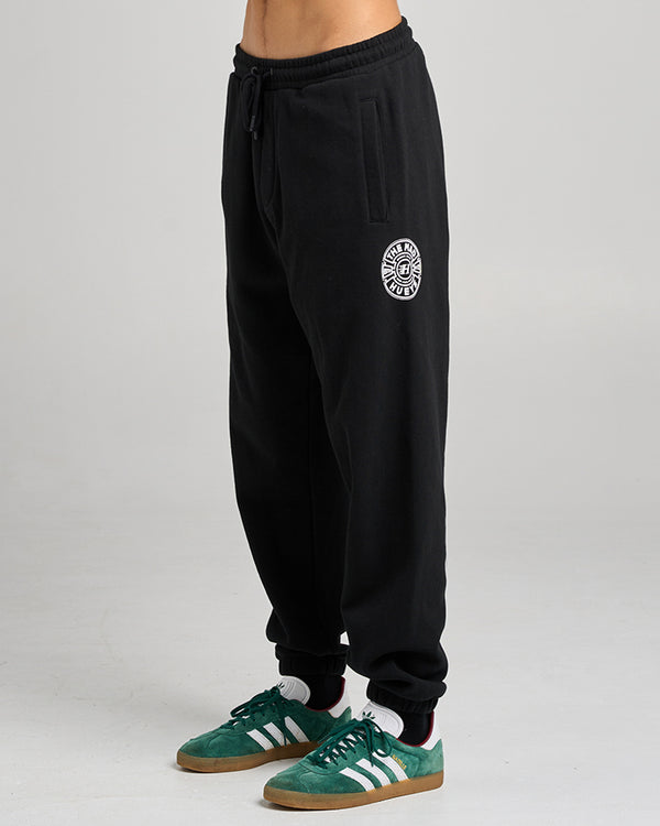 Black jogger pants with The Mad Hueys embroidered logo on the thigh, worn with green Adidas sneakers.