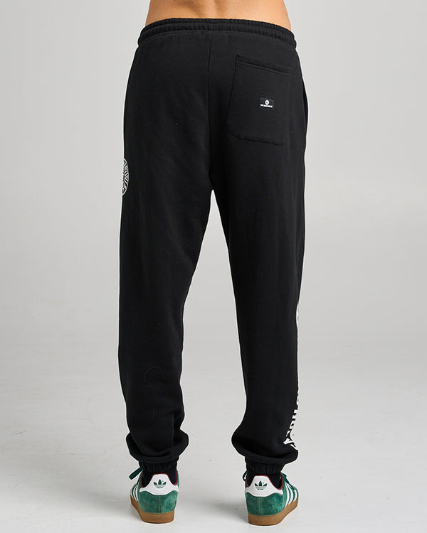 Back view of black jogger pants with a single rear pocket and logo patch, worn with green Adidas sneakers.