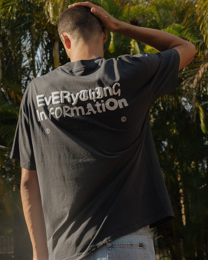 Charcoal oversized t-shirt with "Everything Information" graphic text on the back, worn by a model in an outdoor setting.