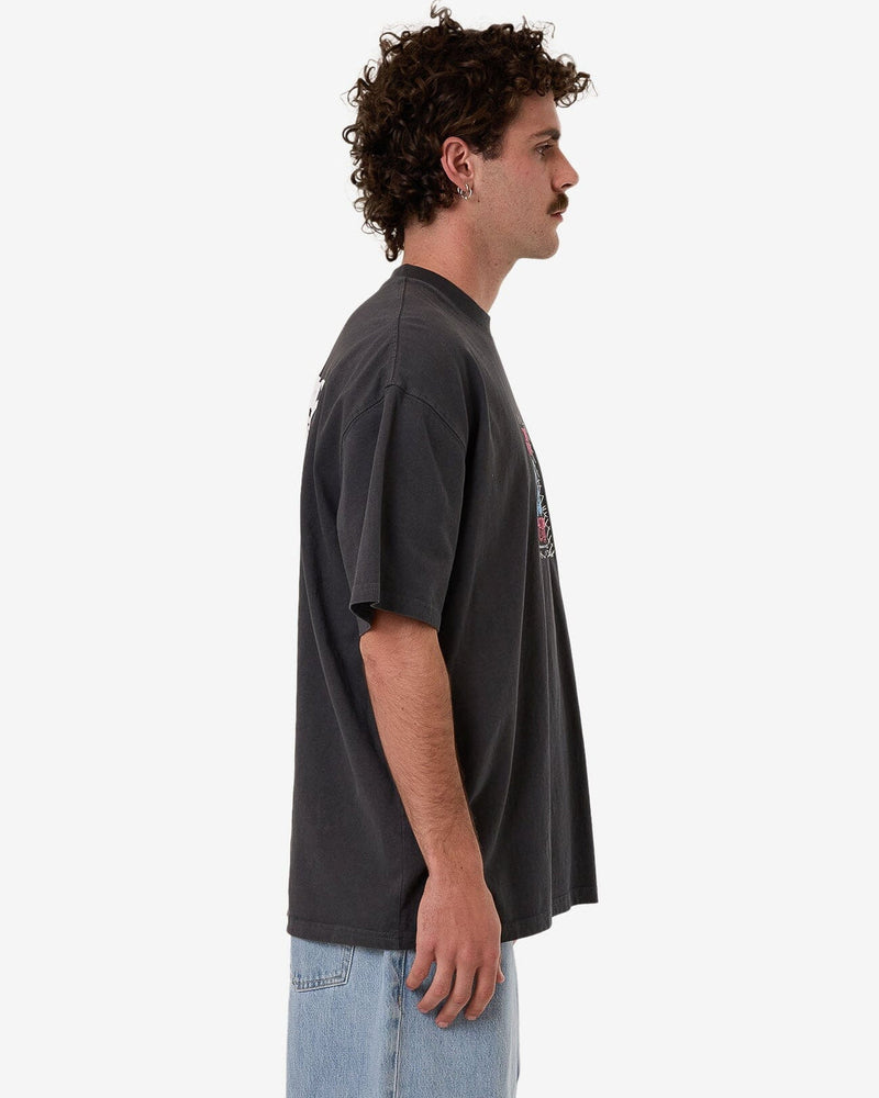 Side view of a model wearing a charcoal oversized graphic t-shirt with short sleeves and a relaxed fit, paired with jeans.