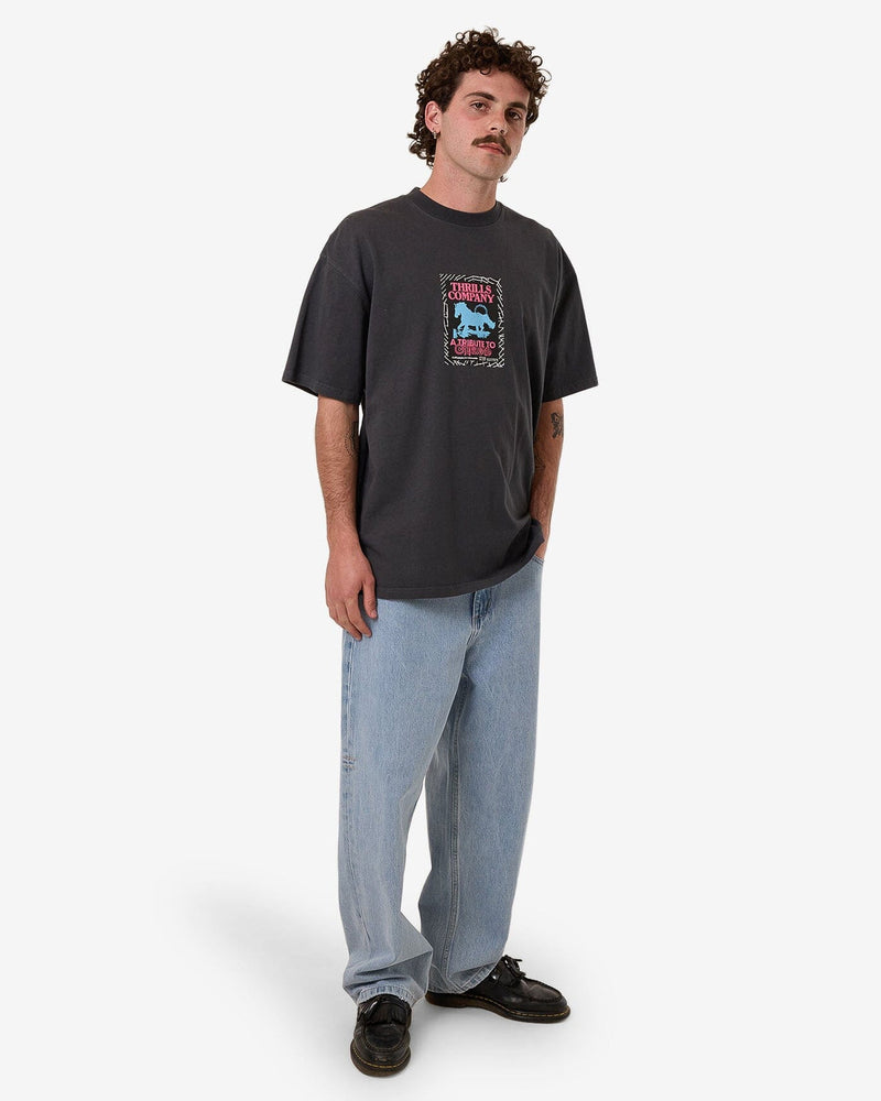 Full-body shot of a model wearing a charcoal oversized graphic t-shirt, light-wash baggy jeans, and black shoes with a relaxed fit.