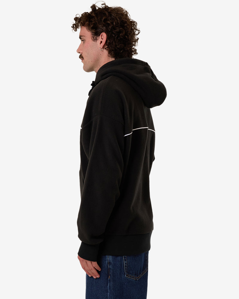 Side view of a black oversized hoodie with a white horizontal stripe, large hood, and ribbed cuffs, paired with denim jeans.