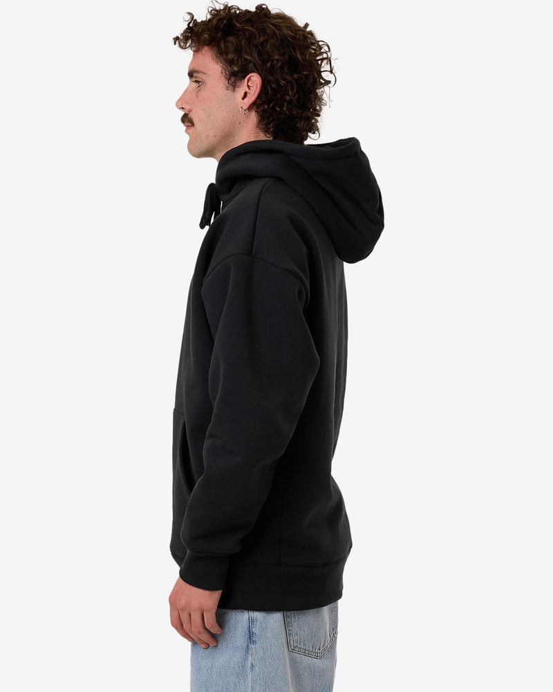 Side view of a black hoodie with an oversized hood and relaxed fit, worn by a model with curly hair and light-wash jeans.