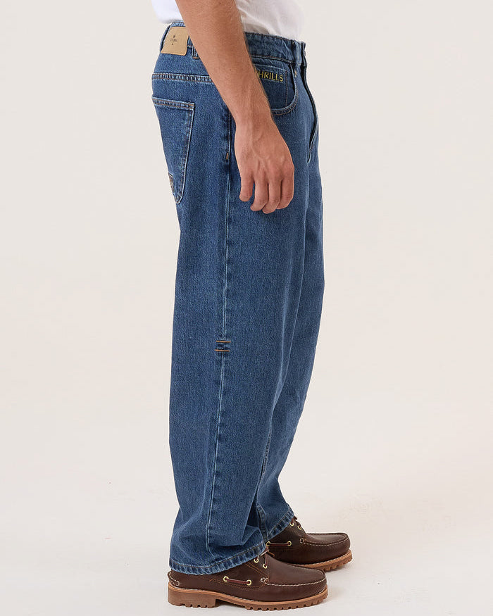 Side view of men's blue denim jeans with a relaxed fit, subtle distressing, and brown leather shoes with a thick sole.