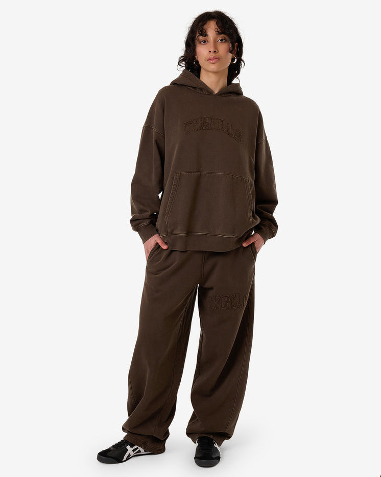 Female model wearing an oversized brown Thrills hoodie and matching wide-leg sweatpants, paired with black sneakers.