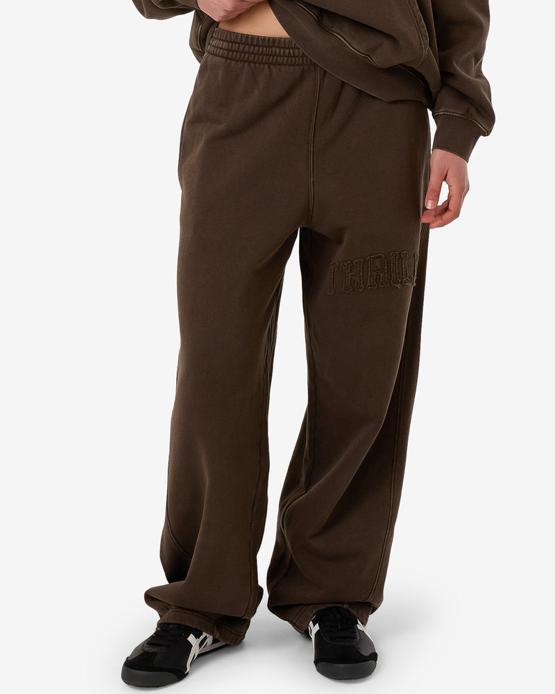 Female model wearing brown Thrills wide-leg sweatpants with embroidered logo on the leg, paired with black sneakers.