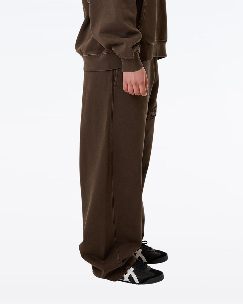 Side view of brown Thrills wide-leg sweatpants with embroidered logo detail, worn with matching hoodie and black sneakers.