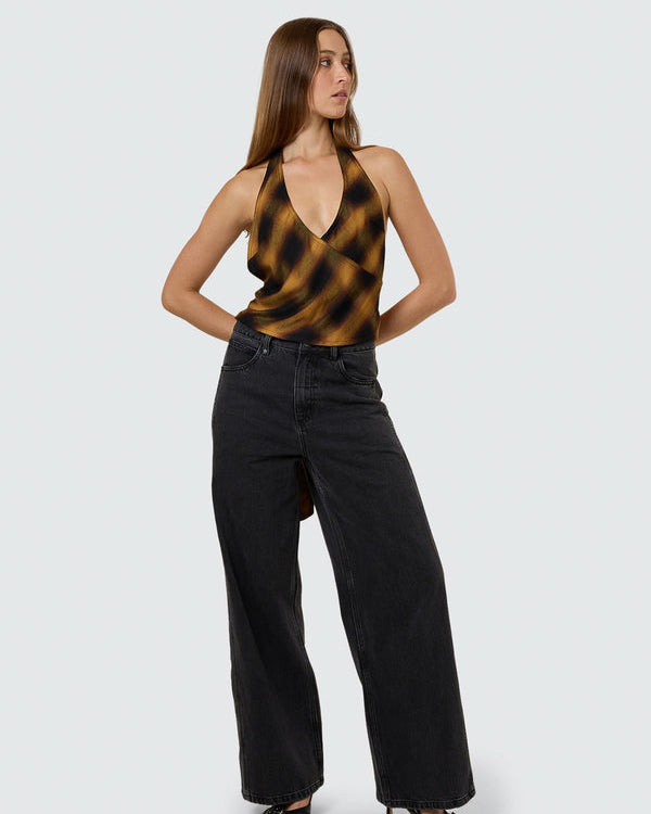 Model striking a pose in a brown and black checkered halter top with a deep V-neck and black wide-leg jeans.