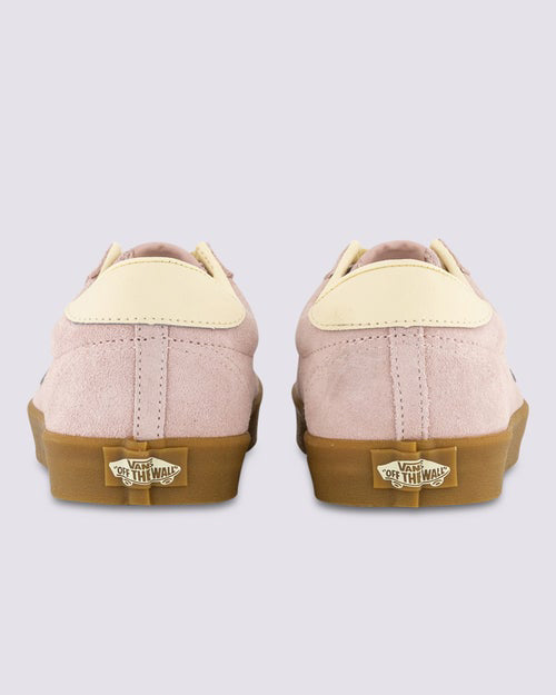 Back view of a pair of Vans sneakers featuring pink suede uppers, cream heel tabs, and brown gum soles with “Off the Wall” branding.
