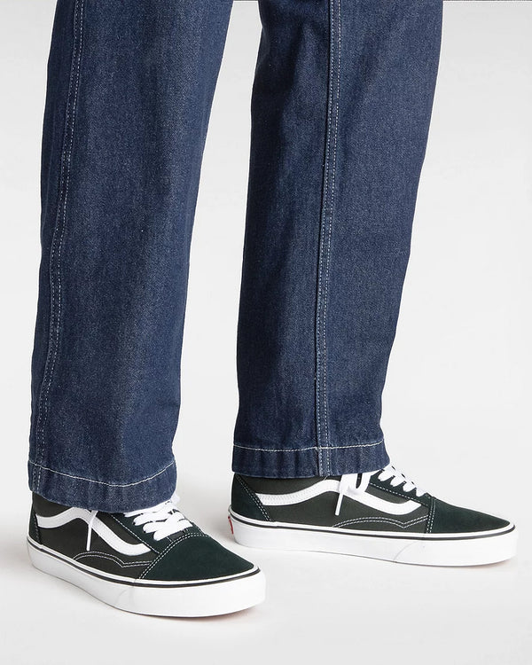 Person wearing dark green Vans Old Skool sneakers with white laces and soles, paired with straight-leg dark denim jeans.