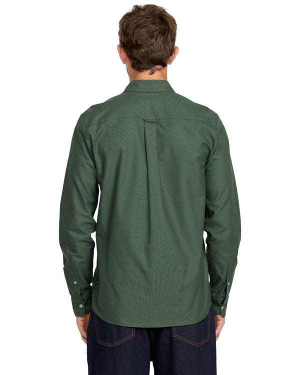 Male model shown from the back wearing a dark green long-sleeve button-up shirt with a pleated back detail and dark jeans.