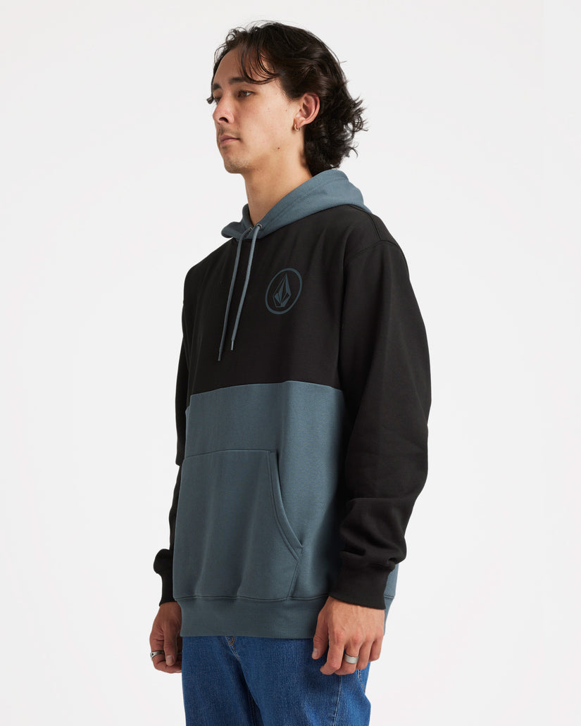 Side view of a male model wearing a two-tone Volcom hoodie with black upper and blue-grey lower half, featuring a logo patch.