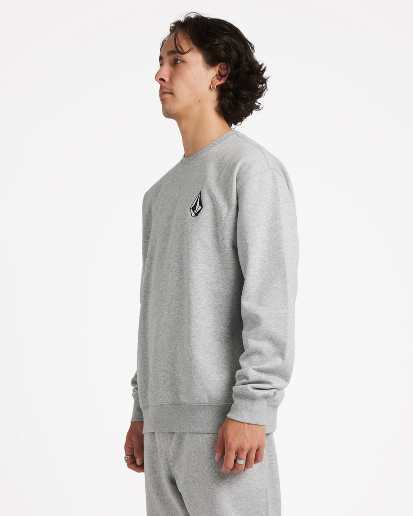 Side view of a male model wearing a light grey crewneck sweatshirt with a small black logo on the chest, paired with sweatpants.