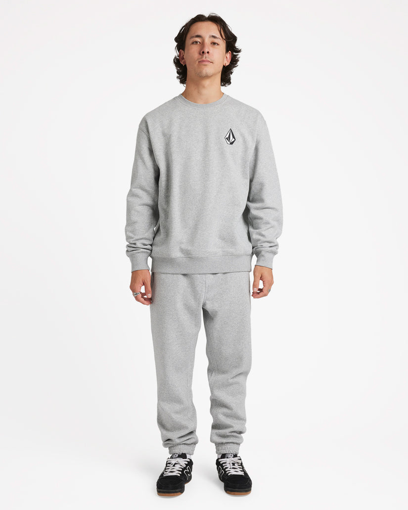 Full-body view of a male model wearing a light grey crewneck sweatshirt with a black logo, matching sweatpants, and sneakers.