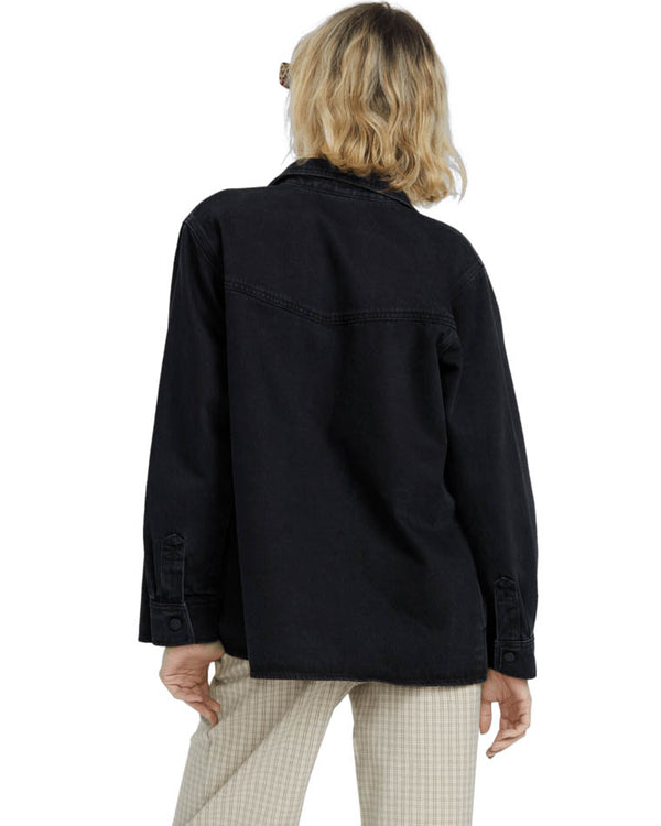 Back view of a model wearing a black oversized denim jacket with beige plaid pants, showing relaxed fit and design details.