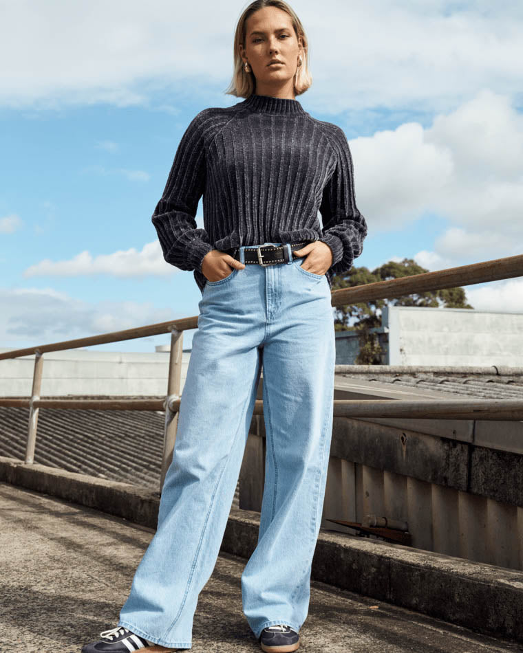 A model wearing high-waisted light blue straight-leg jeans styled with a black ribbed sweater, black belt, and black sneakers.