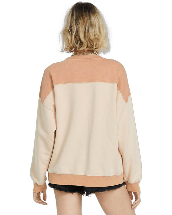 Back view of a woman wearing a color-blocked Volcom Stone sweatshirt in beige and peach tones, paired with black denim shorts.