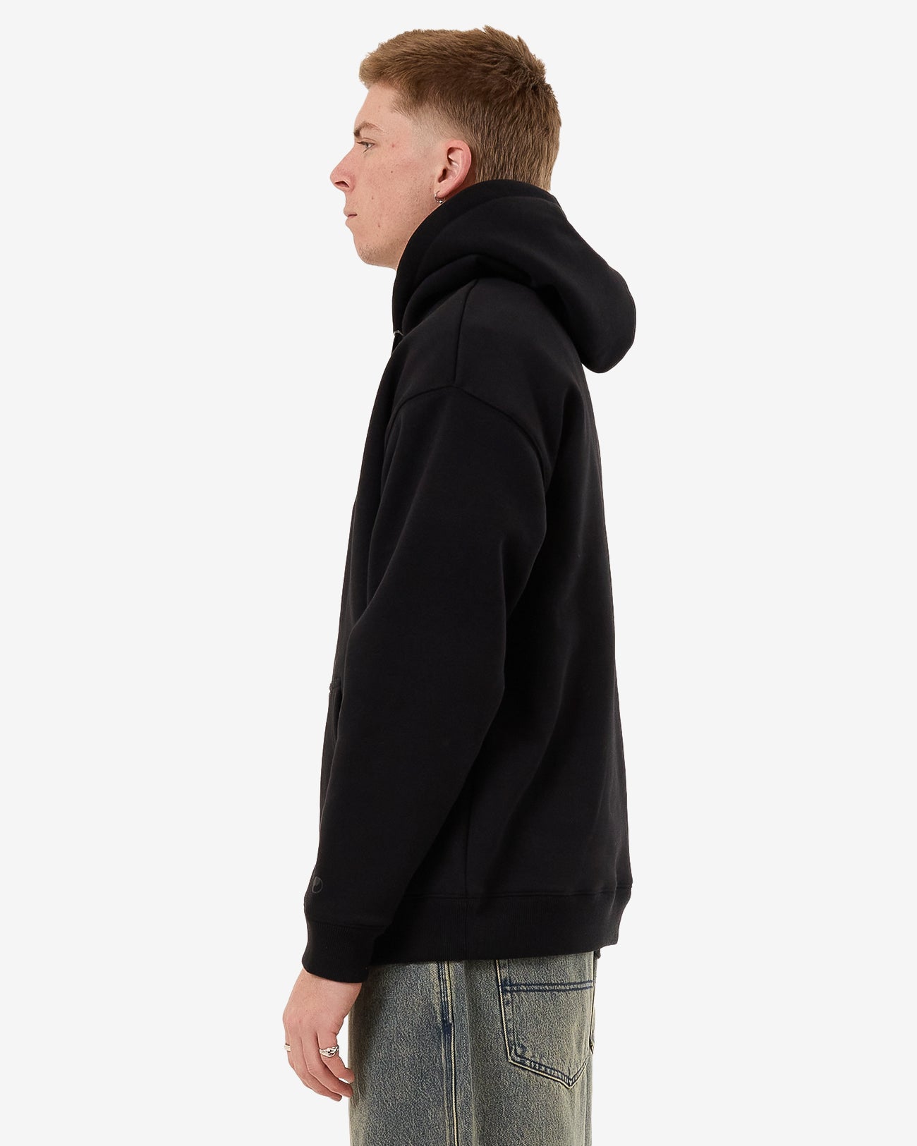 Side view of a black hoodie with an oversized hood, dropped shoulders, and ribbed cuffs, worn by a male model.