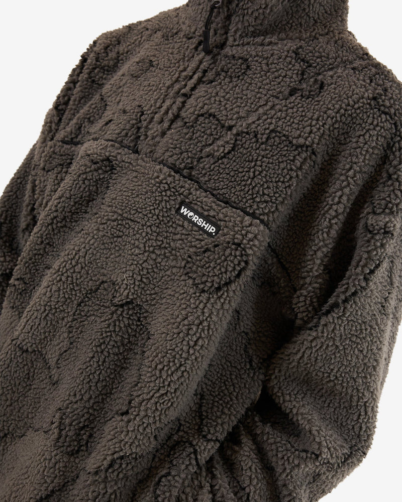 Close-up of a dark grey sherpa fleece pullover with a subtle camouflage pattern, high collar, and a front pocket featuring branding.