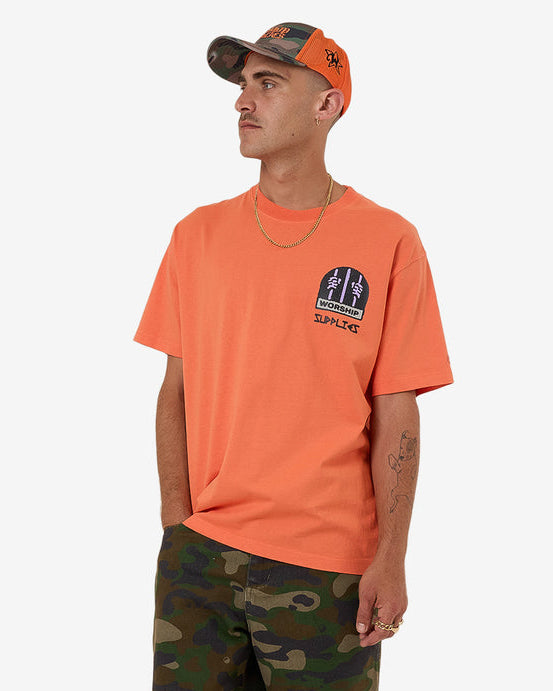 Orange graphic tee styled with camo shorts and cap for casual look