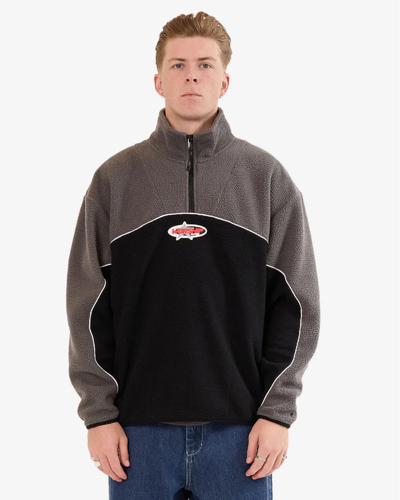 Male model wearing a Worship quarter-zip fleece in black and grey with white piping detail and red logo patch on the chest.