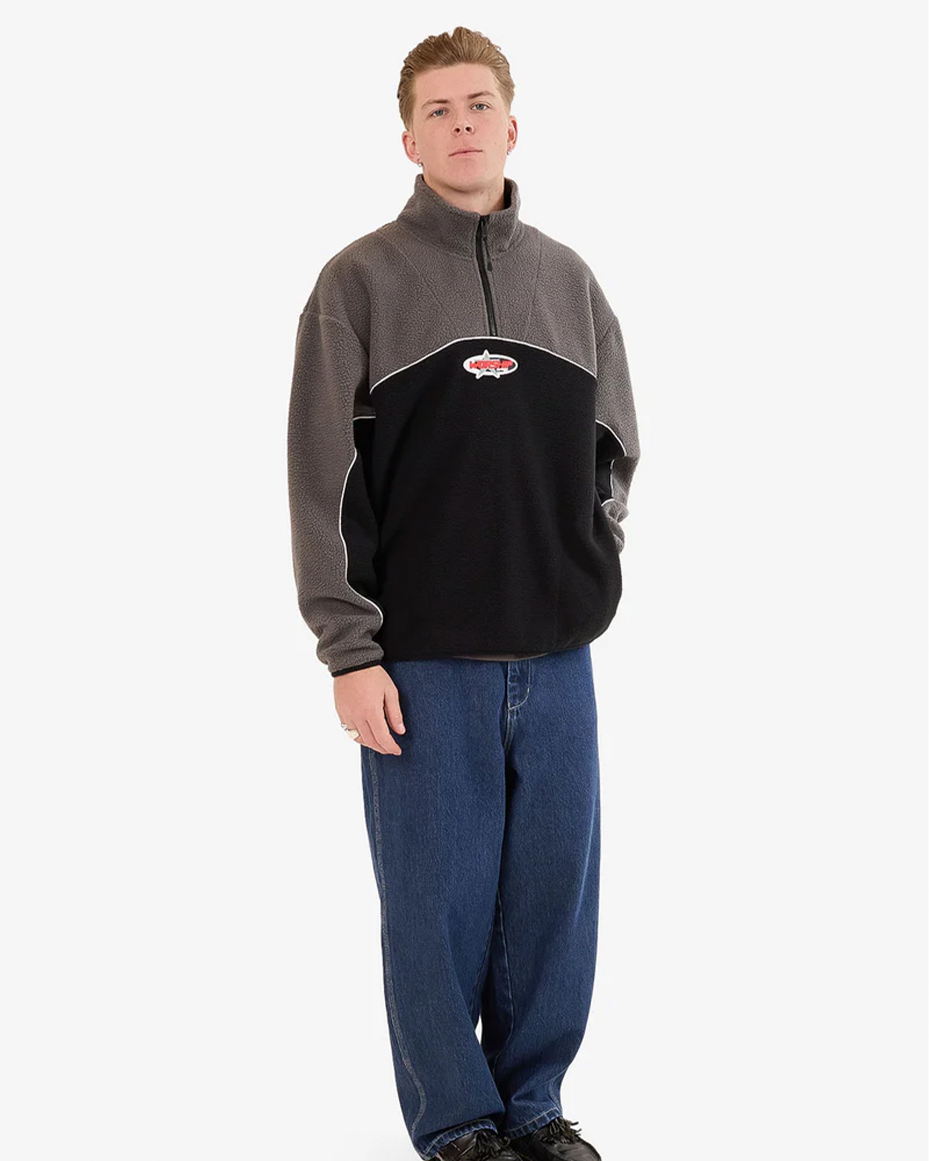 Full body shot of a male model wearing the Worship quarter-zip fleece paired with baggy blue jeans and black sneakers.