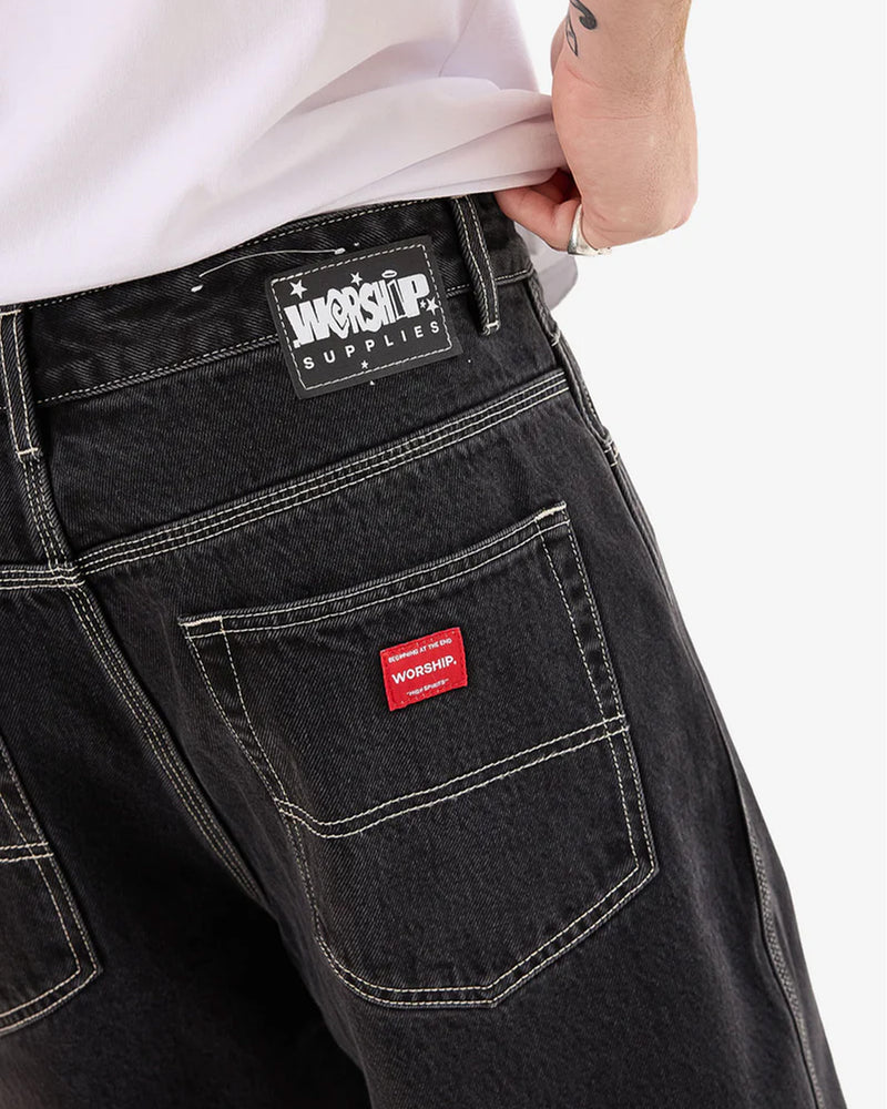 Close-up of Worship branding details on the back waistband and pocket of black jeans.