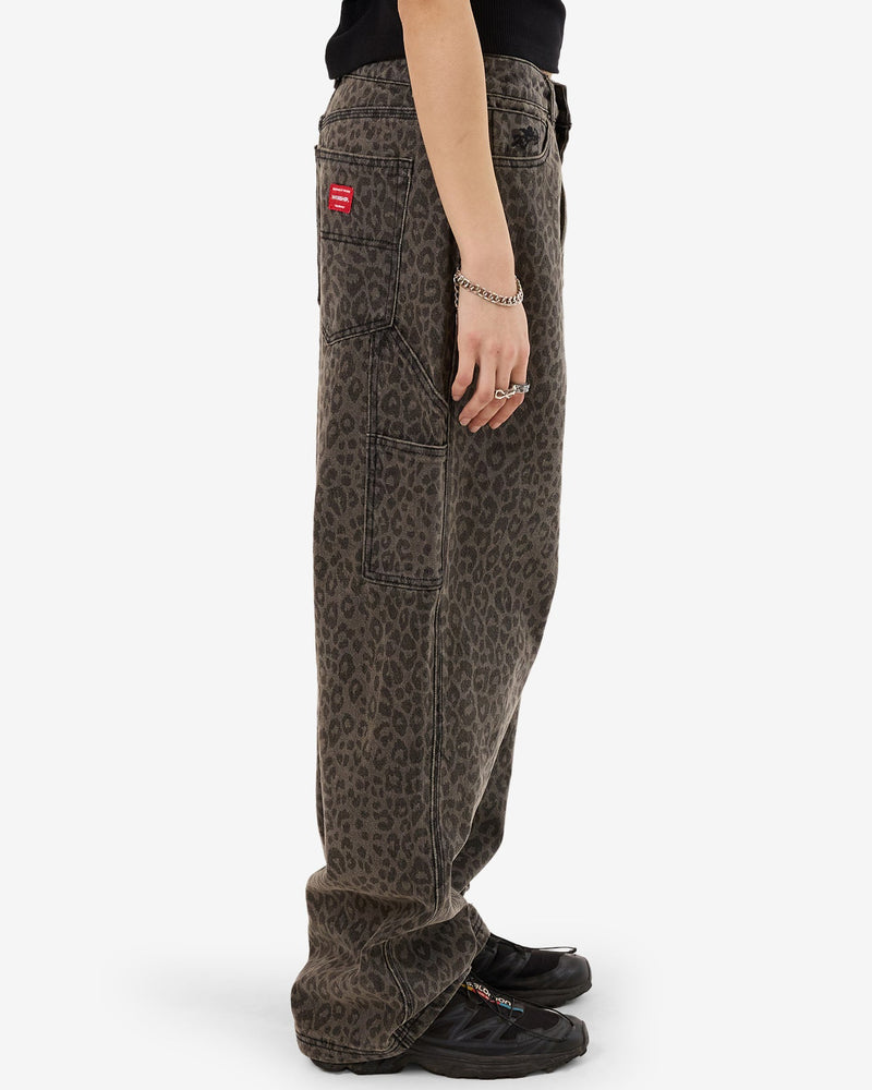 Side view of baggy, wide-leg leopard print jeans with utility side pocket, patch pockets, and red logo tag detail.