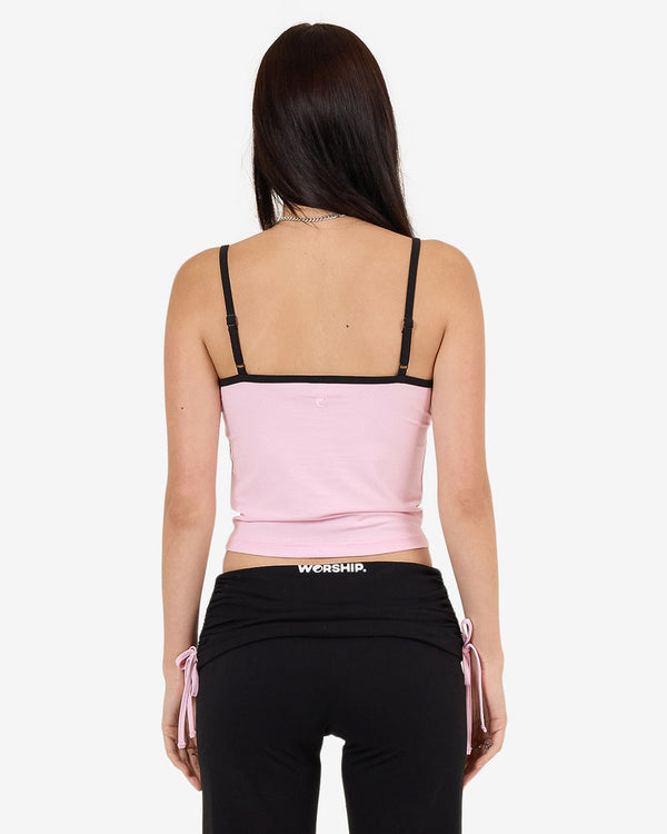 Back view of pink cropped tank top with black straps and "Worship" logo, worn with black drawstring pants.