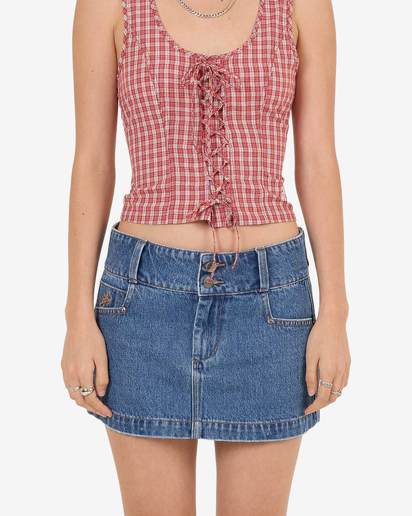 Front view of blue denim mini skirt with belt loops and button closure, paired with red check lace-up top