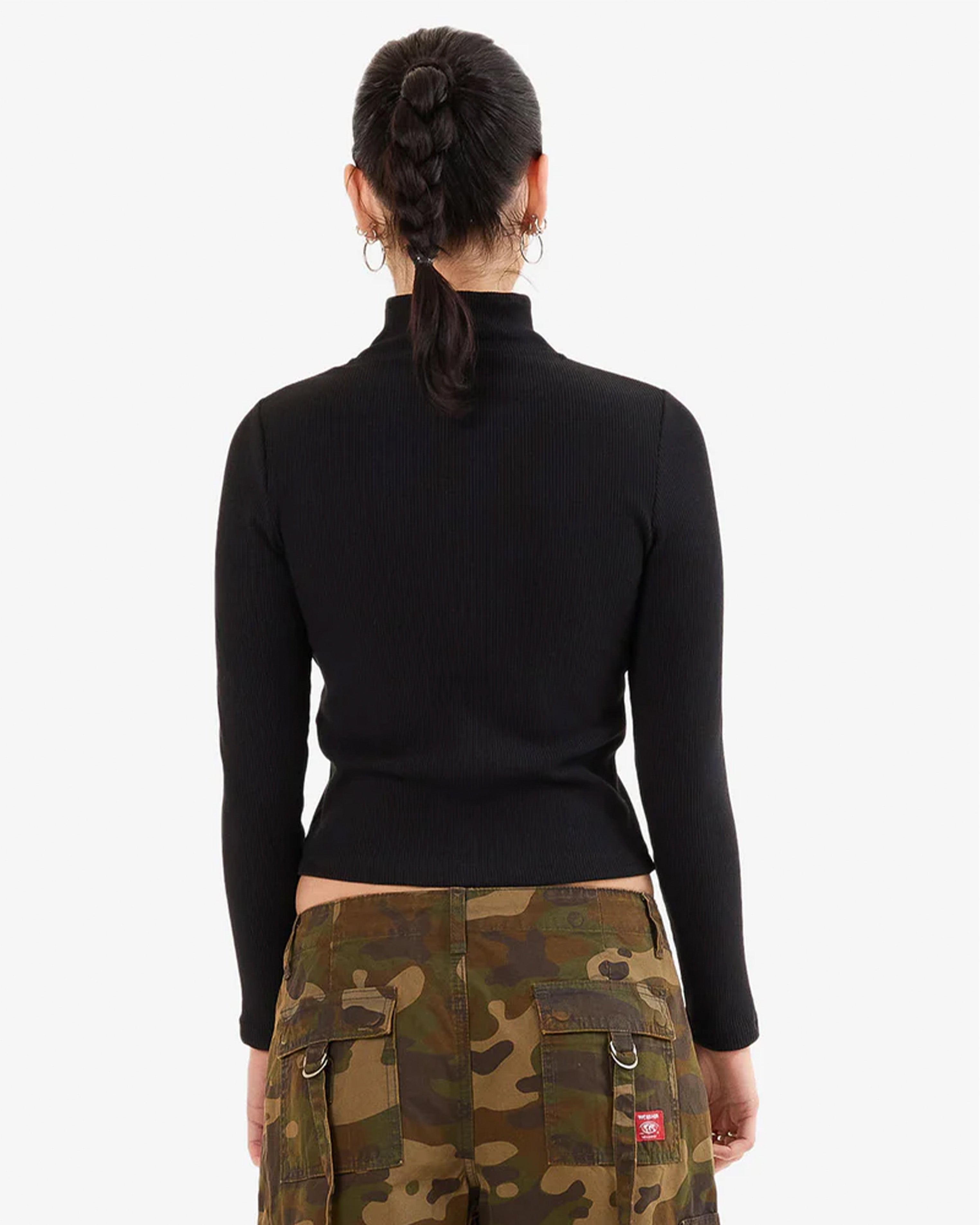 Woman back view wearing a fitted black long sleeve zip-up top and camo cargo pants, with hoop earrings and a braided ponytail.
