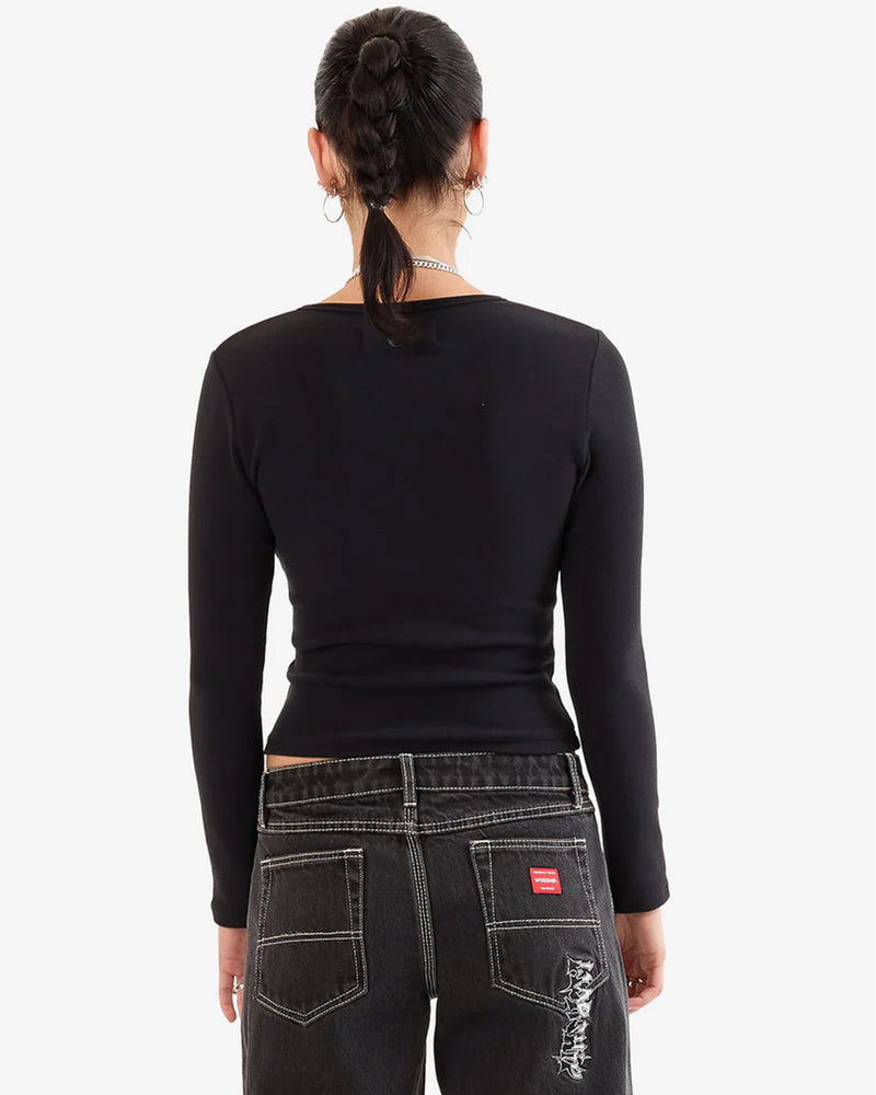 Back view of a woman wearing a fitted black long sleeve top paired with black jeans featuring white contrast stitching and back pocket embroidery.