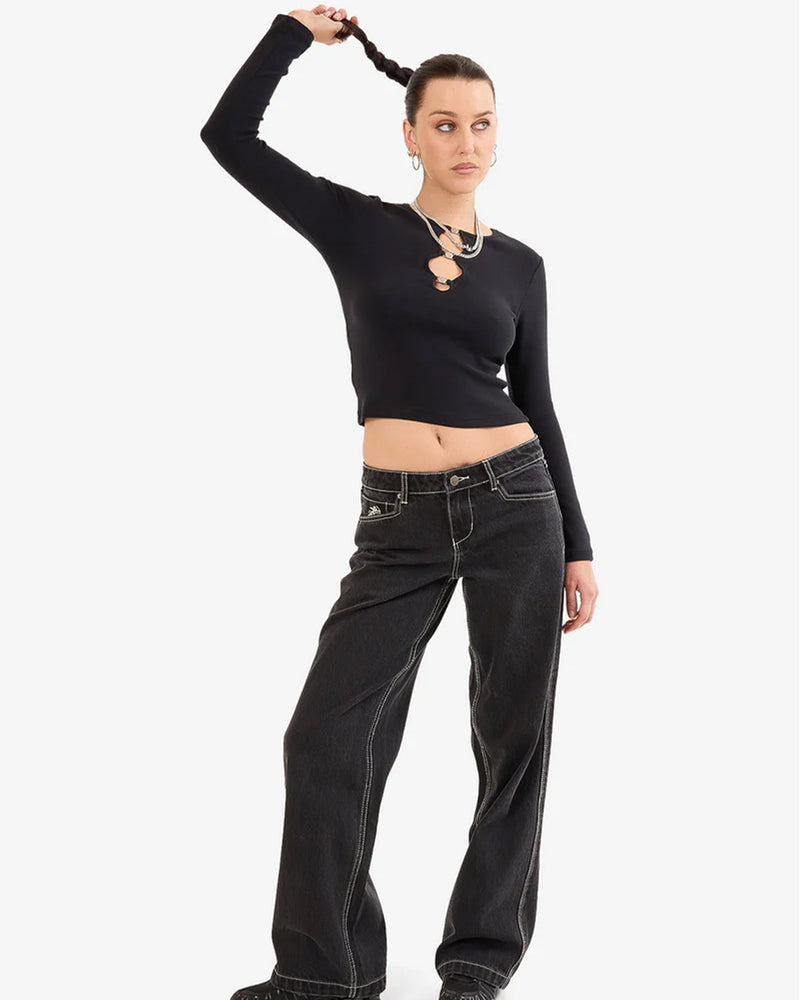 Front view of a woman wearing a fitted black long sleeve top with circular cut-out details and loose black jeans with contrast stitching.