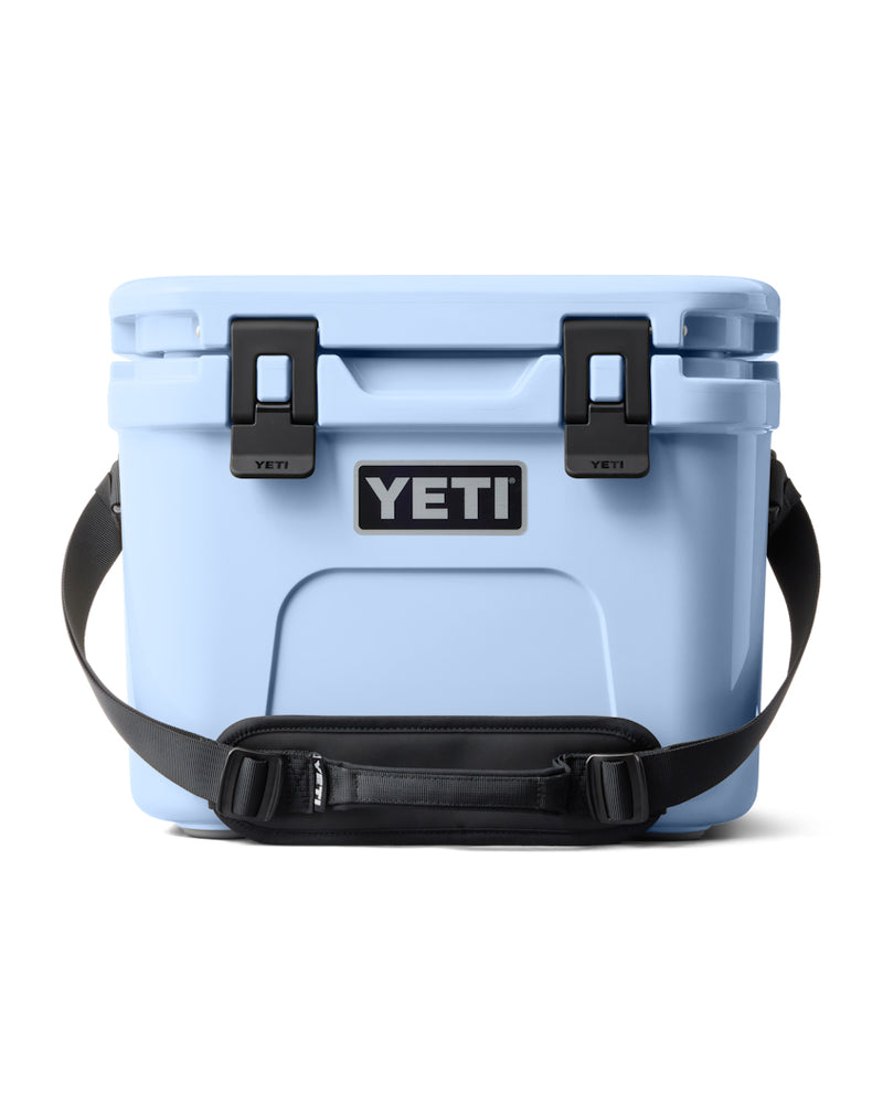 Light blue YETI hard cooler with black latches, a sturdy carrying strap, and a durable design for outdoor use.